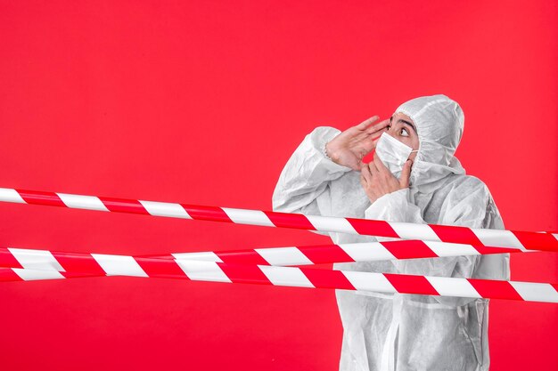 Front view male doctor in protective suit and mask on red background virus isolation covid- cure hospital quarantine color