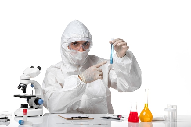 Front view male doctor in protective suit with mask due to covid holding flask with blue solution on light-white space