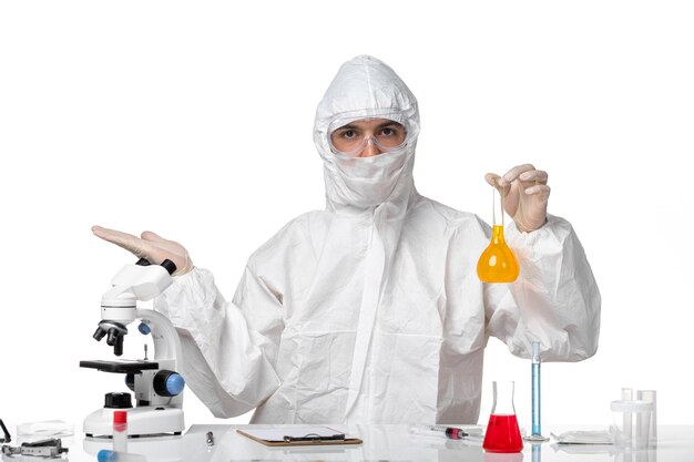 Front view male doctor in protective suit with mask due to covid holding flask with yellow solution on a white space