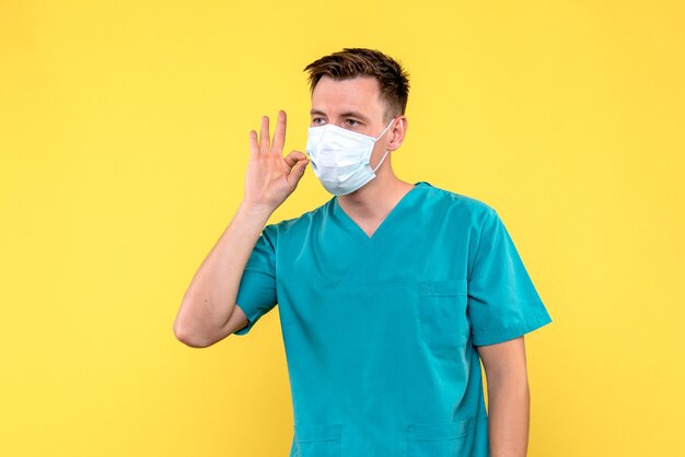 Front view of male doctor in sterile mask on a yellow wall