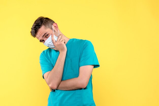 Front view of male doctor in sterile mask on yellow wall