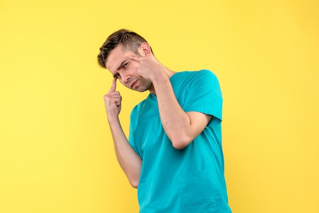 Front view of male doctor thinking on a yellow wall