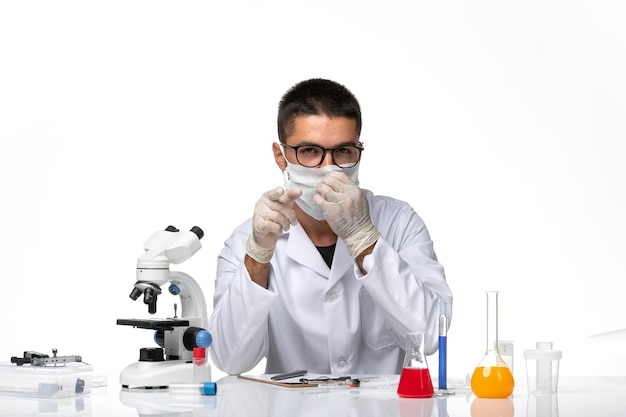 Front view male doctor in white medical suit with mask due to covid on a white space