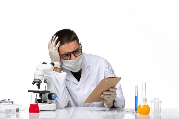 Front view male doctor in white medical suit with mask due to covid writing notes on the white space