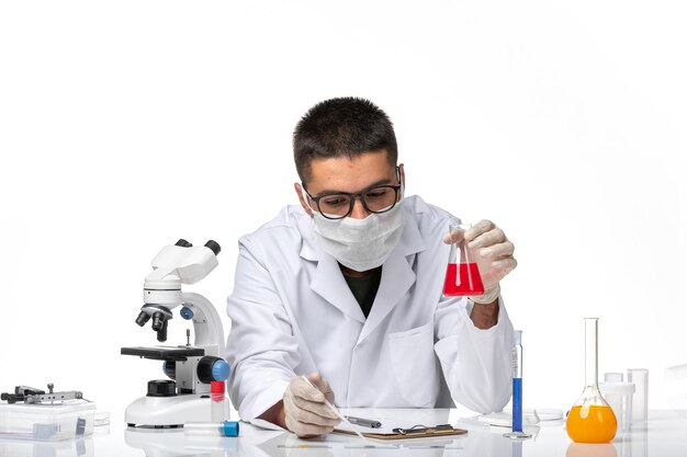 Front view male doctor in white medical suit and with mask working with solution on light white space