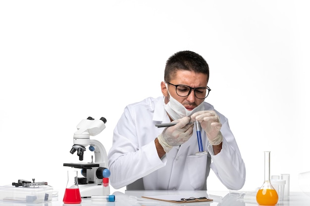 Front view male doctor in white medical suit and with mask working with solution on white space