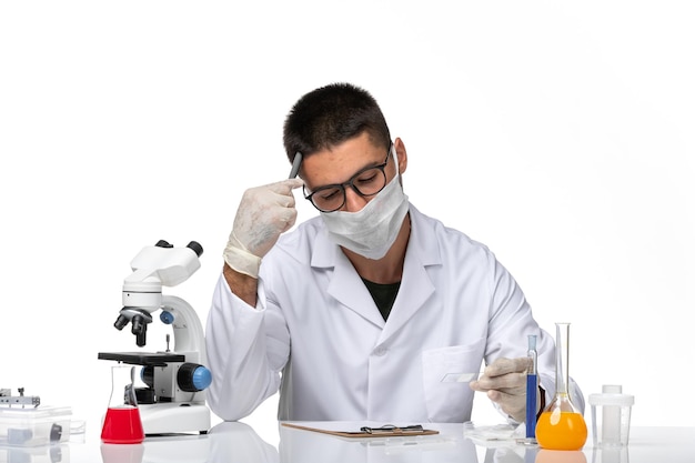 Front view male doctor in white medical suit working and writing on white space