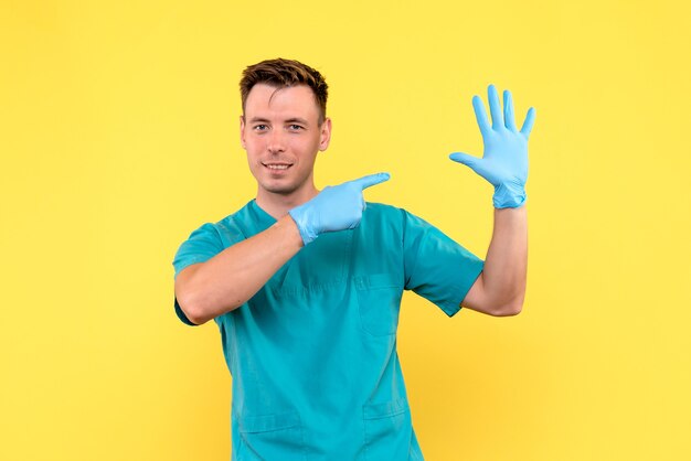 Front view of male doctor with blue gloves on yellow floor hospital medical emotion