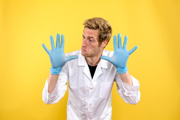 Free photo front view male doctor with gloves on a yellow background medic covid- health hygiene