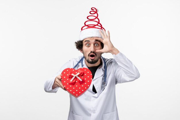 Front view of male doctor with holiday present on a white wall