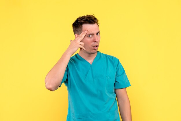 Front view of male doctor with thinking expression on yellow wall