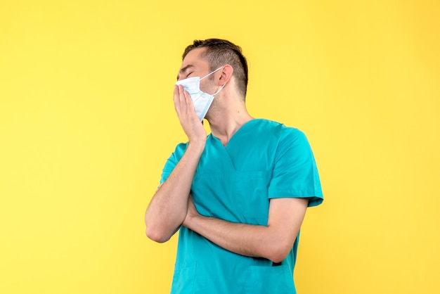 Front view of male doctor yawning in sterile mask on yellow wall