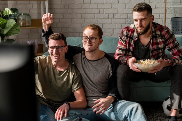 Front view of male friends watching sports on tv and having snacks together