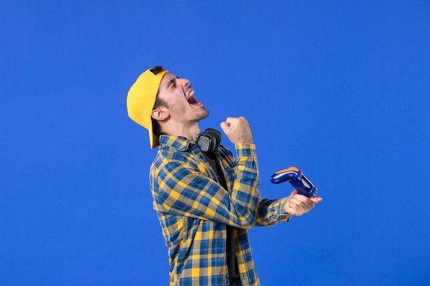 Front view of male gamer with gamepad playing video game on blue wall