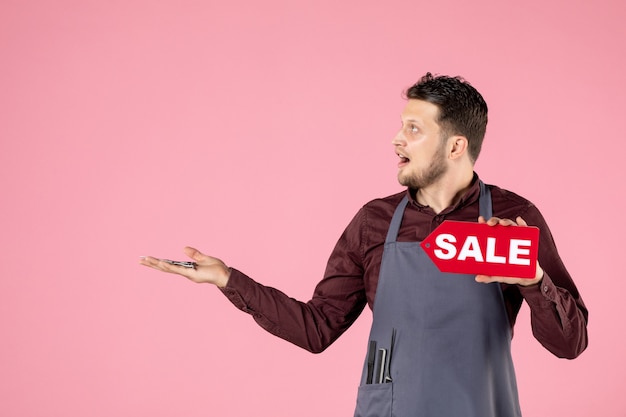 front view male hairdresser with sale nameplate and scissors on pink background