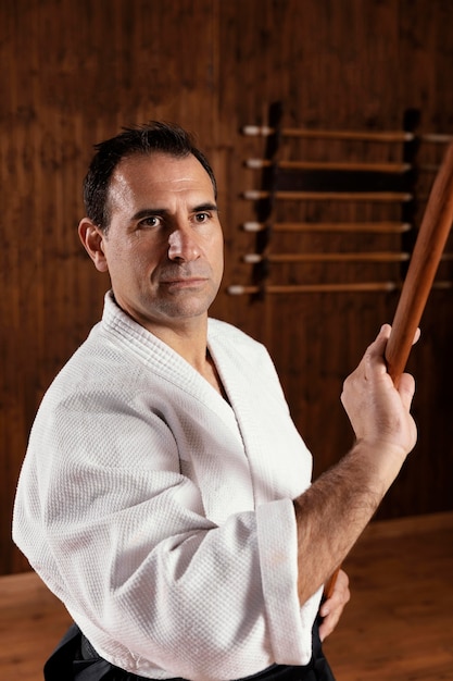 Front view of male martial arts instructor in the practice hall with wooden stick