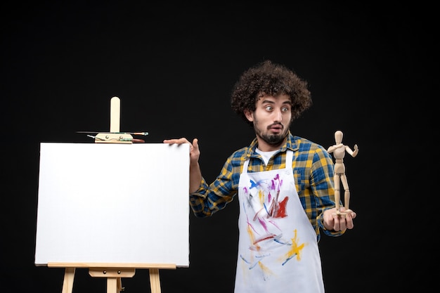 Free Photo front view male painter with easel holding human figure on black table