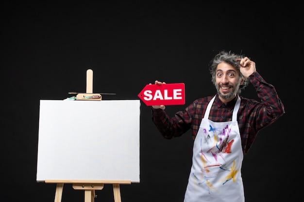 Free Photo front view of male painter with easel holding sale banner on dark wall