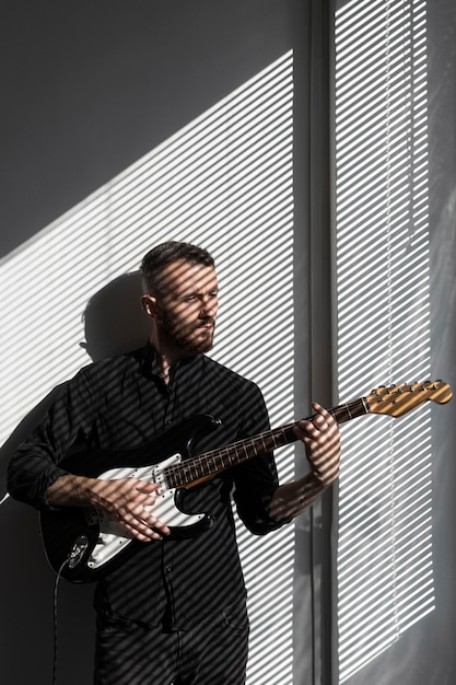 Free Photo front view of male performer posing next to window while playing electric guitar