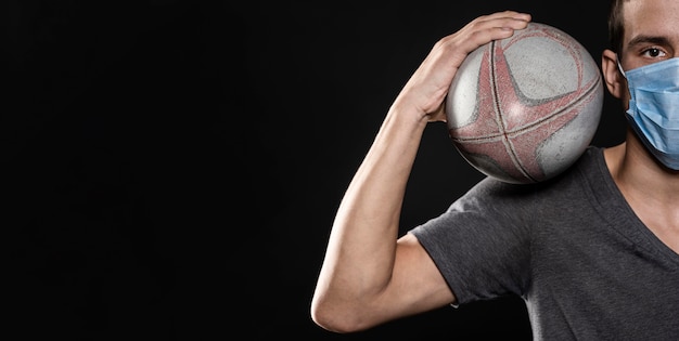 Front view of male rugby player with medical mask and ball