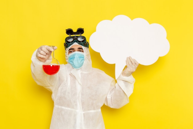 Free photo front view male scientific worker in special protective suit holding flask with red solution and big white sign on yellow desk