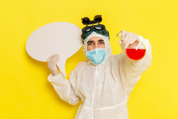 Free photo front view male scientific worker in special protective suit holding flask with red solution and white sign on yellow surface