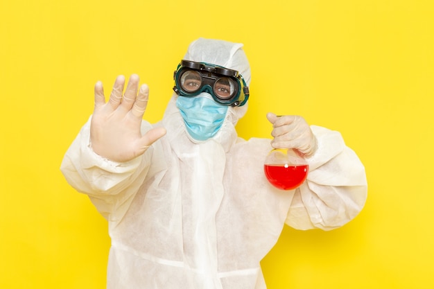 Front view male scientific worker in special protective suit holding flask with red solution on the yellow desk