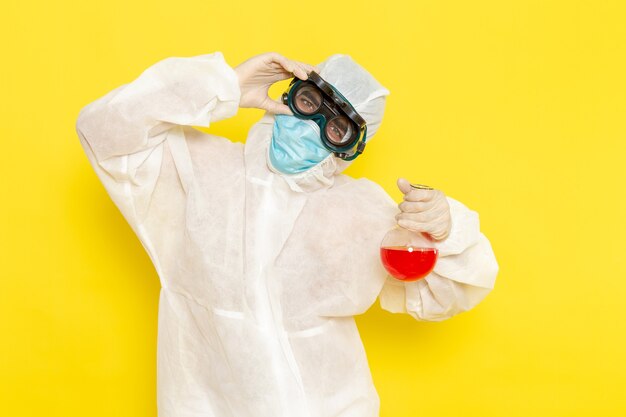 Front view male scientific worker in special protective suit holding flask with red solution on yellow desk