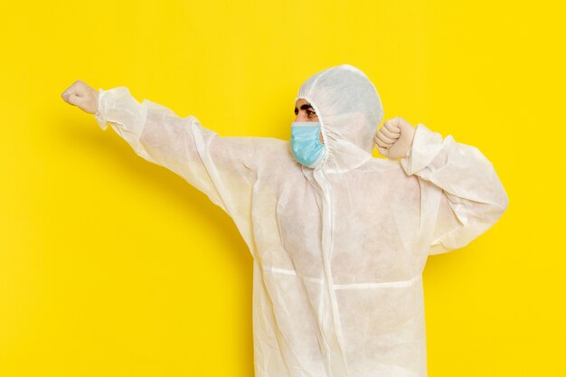 Front view of male scientific worker in special protective suit and with mask just posing on light yellow wall