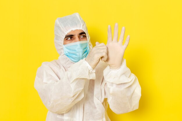 Free photo front view of male scientific worker in special protective suit and with mask wearing gloves on yellow wall