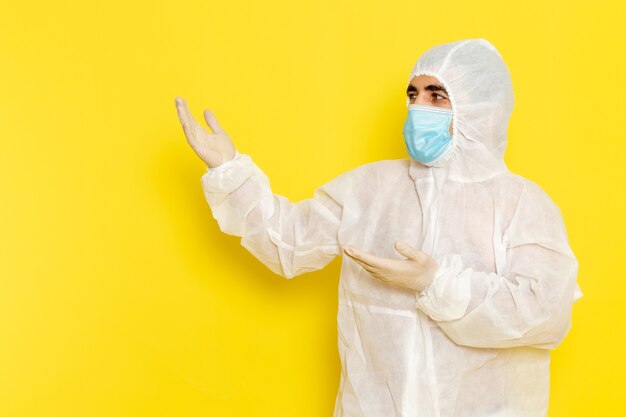 Front view of male scientific worker in special protective white suit with mask on light-yellow wall