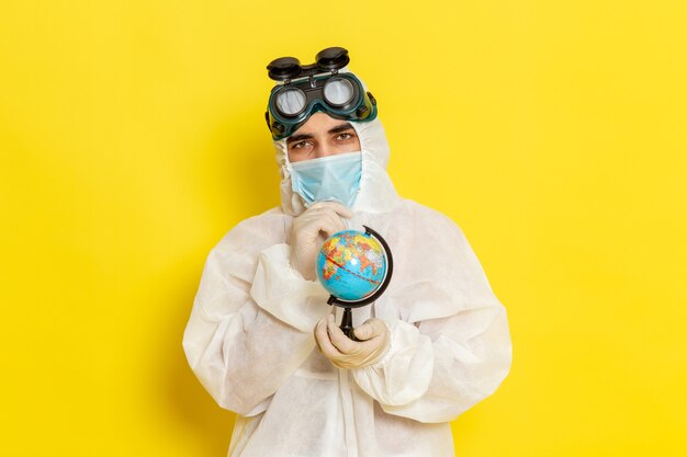 Front view male scientific worker in special suit holding little globe on yellow desk