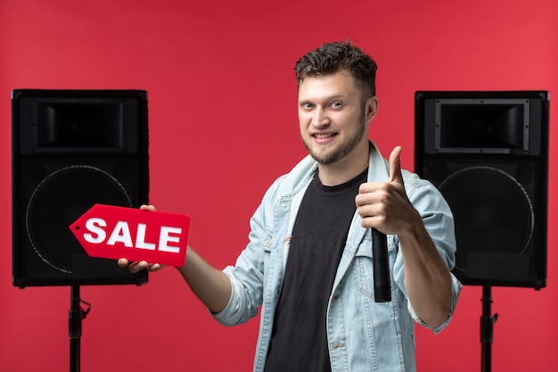 Free photo front view of male singer performing on stage holding red sale writing on light red wall