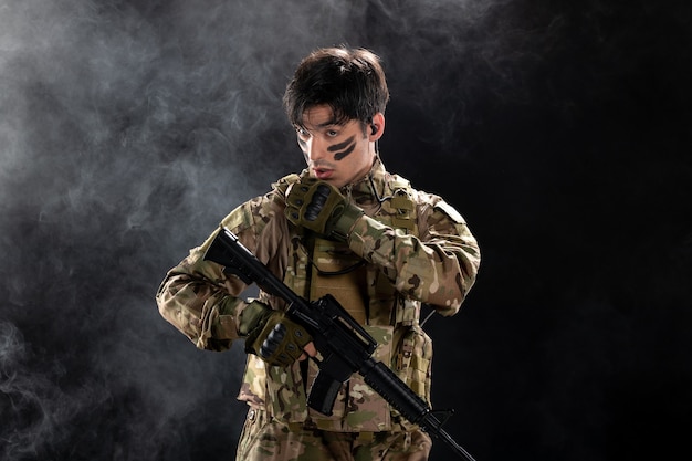 Front view of male soldier in camouflage aiming rifle on a black wall