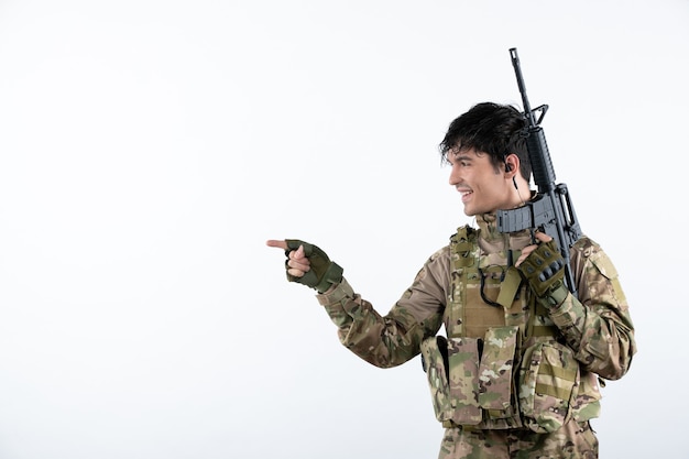 Front view of male soldier with machine gun in camouflage white wall