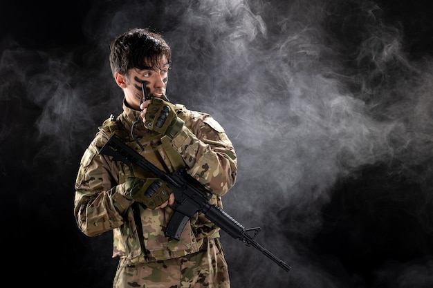 Front view of male soldier with machine gun using walkie-talkie black wall