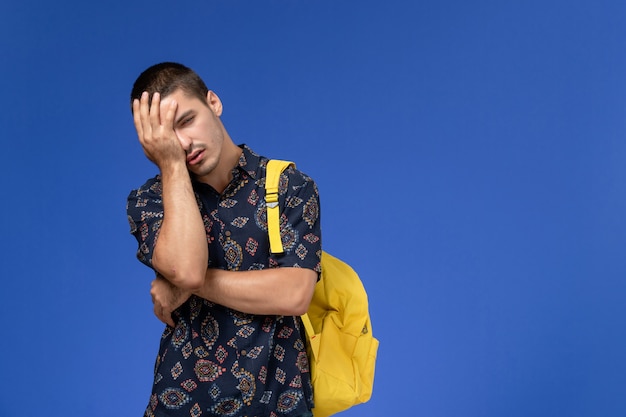 Front view of male student in dark cotton shirt wearing yellow backpack tired boy on light blue wall