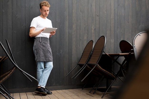 Front view of male waiter with apron and tablet