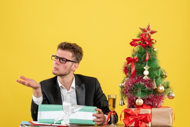 Front view male worker behind his working place with different presents on yellow 