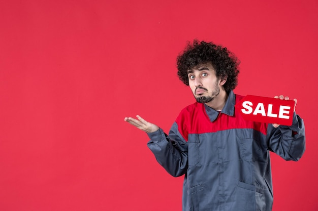 Free photo front view male worker holding red sale nameplate on red background mechanic photo house color shopping job worker uniform instrument