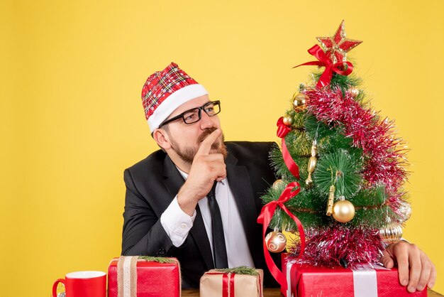 Front view male worker sitting behind his working place with presents thinking on yellow 