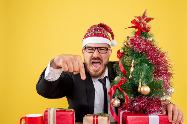 Front view male worker sitting behind his working place with presents on a yellow 