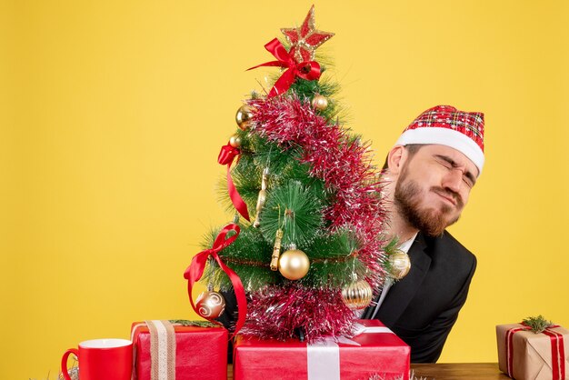 Front view male worker sitting behind his working place with presents on yellow 