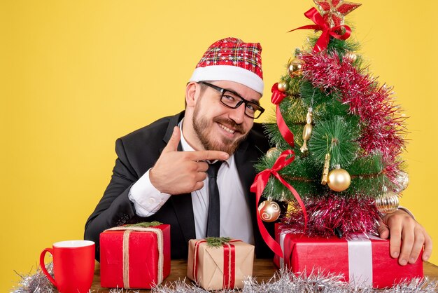 Front view male worker sitting behind his working place with presents on yellow 