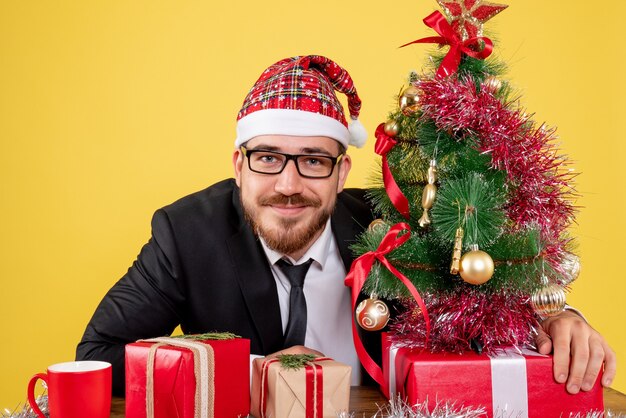 Front view male worker sitting behind his working place with presents on yellow 