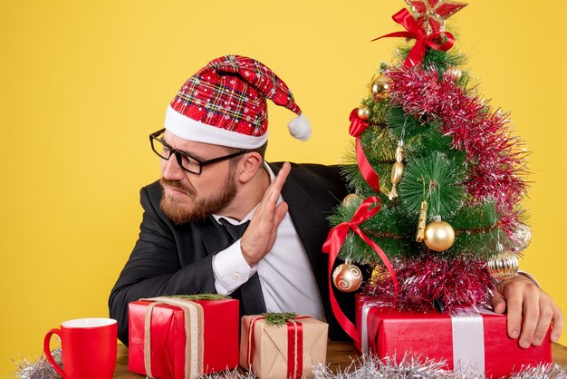 Front view male worker sitting behind his working place with presents on yellow 