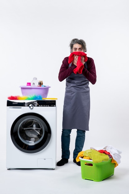 Front view man in apron wiping his face with towel standing near washer on white wall