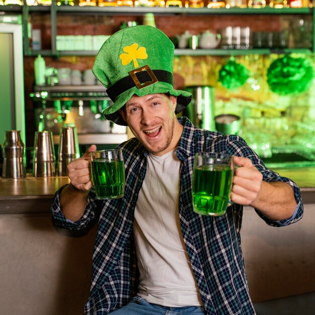 Front view of man celebrating st. patrick's day at the bar with drinks