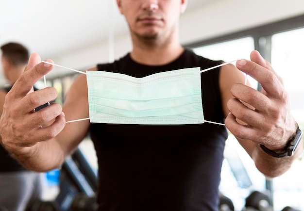 Front view of man at the gym holding medical mask during the pandemic