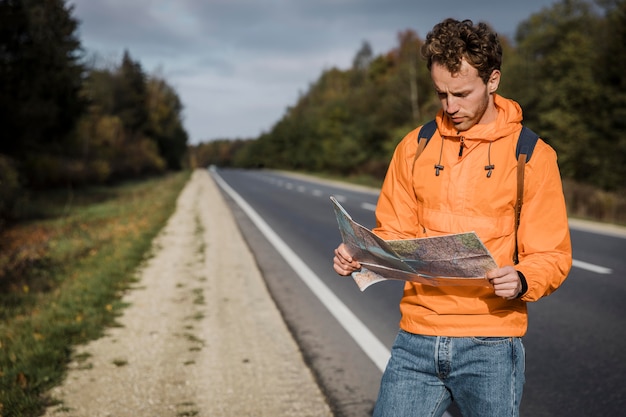 Free photo front view of man holding map and sitting along the road